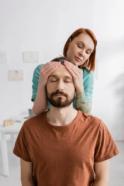 Physiotherapist examining injured bearded man in consulting room — Stock Photo