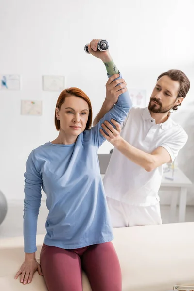 Physiotherapeutin unterstützt Arm von Frau beim Training mit Hantel im Reha-Zentrum — Stockfoto