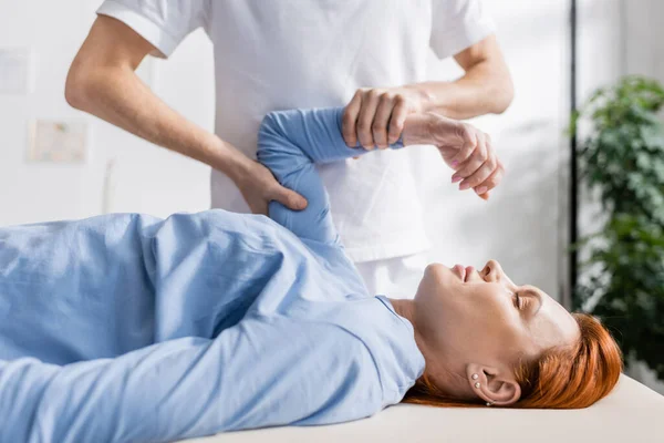 Chiropractor flexing injured arm of redhead woman in rehabilitation clinic — Stock Photo