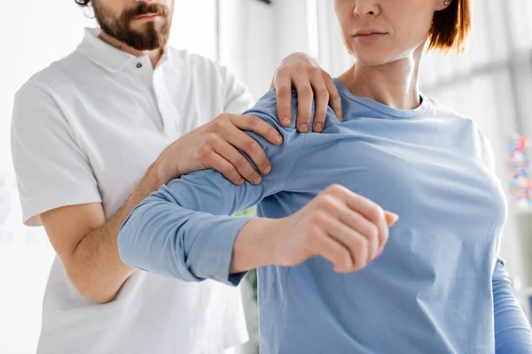 Vue partielle du chiropraticien examinant l'épaule douloureuse de la femme dans la salle de consultation — Photo de stock