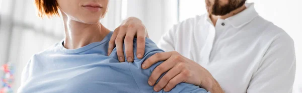 Partial view of rehabilitologist examining injured shoulder of patient in consulting room, banner — Stock Photo