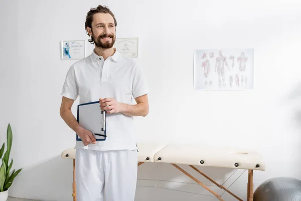 Счастливый физиотерапевт держит планшет с чистой бумагой и смотрит в реабилитационный центр — стоковое фото
