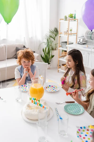 Vista de ángulo alto de niños alegres sosteniendo cuernos de fiesta durante el cumpleaños en casa - foto de stock