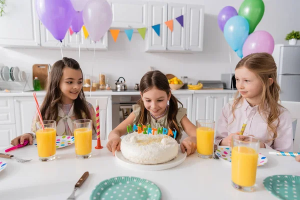 Счастливая девушка смотрит на именинный торт со свечами рядом с друзьями во время празднования дома — стоковое фото