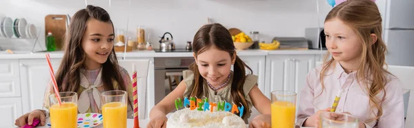 Счастливая девушка смотрит на именинный торт со свечами рядом с друзьями во время празднования дома, баннер — стоковое фото