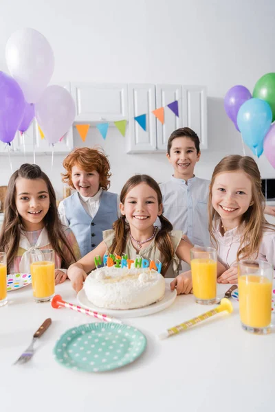 Group of happy boys and girls celebrating birthday party next to tasty cake at home — Stock Photo