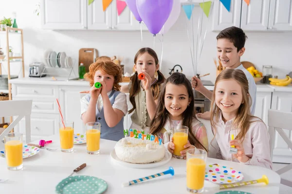 Группа счастливых мальчиков и девочек, дующих в рога во время празднования дня рождения дома — стоковое фото
