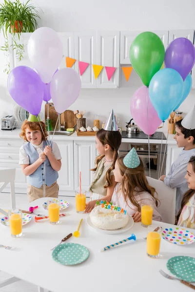 Щасливий рудий хлопчик тримає повітряні кулі біля друзів під час дня народження вдома — стокове фото