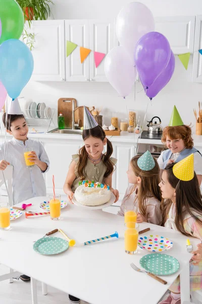 Grupo de niños felices en gorras de fiesta divirtiéndose durante el cumpleaños en casa - foto de stock