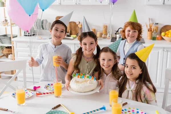 Grupo de niños alegres en gorras de fiesta divirtiéndose durante el cumpleaños en casa - foto de stock