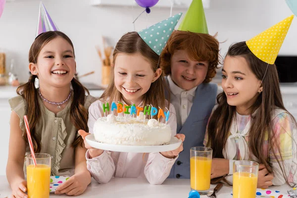Щаслива дівчина з днем народження тримає торт зі свічками біля веселих друзів під час святкування вдома — стокове фото