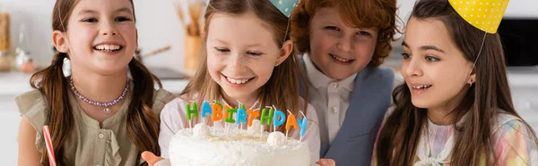 Glückliches Geburtstagskind mit Kuchen und Kerzen bei fröhlichen Freunden während der Feier zu Hause, Banner — Stockfoto