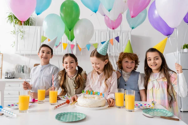 Grupo de niños alegres divirtiéndose durante la fiesta de cumpleaños junto a globos en casa - foto de stock