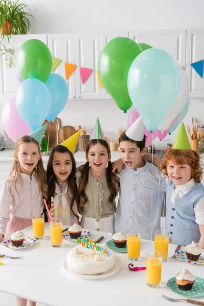 Grupo de niños cantando feliz cumpleaños junto a cupcakes y globos - foto de stock