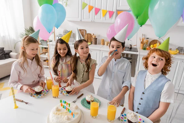 Niñas preadolescentes felices sosteniendo cupcakes y mirando a los niños durante la fiesta de cumpleaños - foto de stock