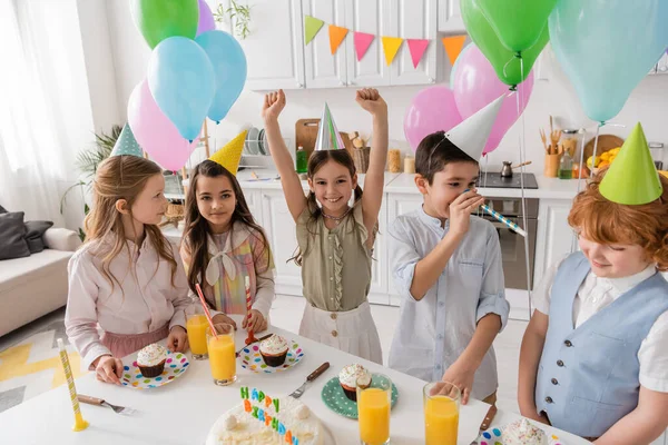 Grupo y niños felices en gorras de fiesta divirtiéndose durante el cumpleaños en casa - foto de stock