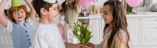 Heureux garçon donner tulipes à joyeux anniversaire fille près d'amis sur fond flou, bannière — Photo de stock