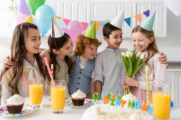 Alegre cumpleaños chica celebración tulipanes cerca amigos durante la celebración en casa - foto de stock