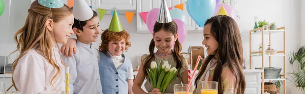 Alegre cumpleaños chica celebración tulipanes cerca alegre amigos durante la celebración en casa, pancarta - foto de stock