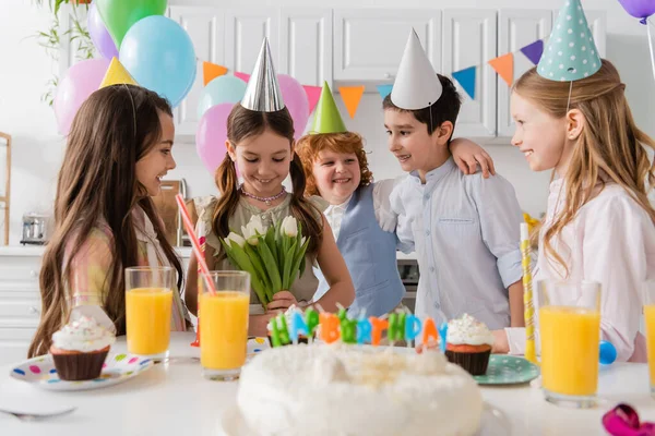 Веселая девушка держит тюльпаны рядом с друзьями во время празднования дня рождения дома — стоковое фото