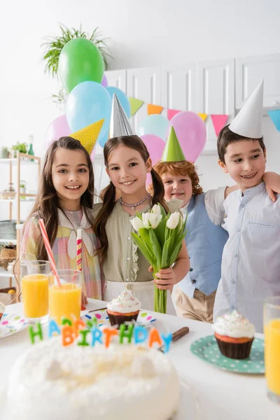 Весела дівчина тримає тюльпани біля позитивних друзів під час святкування дня народження вдома — стокове фото