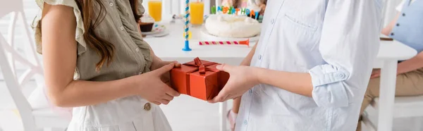 Recortado vista de niño preadolescente dando regalo a chica de cumpleaños cerca de amigos sobre fondo borroso, bandera - foto de stock