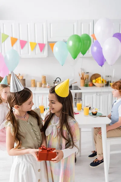Cheerful preteen girl congratulating friend with happy birthday while holding gift box — Stock Photo