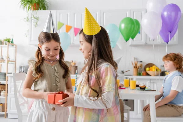 Девочка-подросток поздравляет довольного друга с днем рождения, держа в руках подарочную коробку — стоковое фото