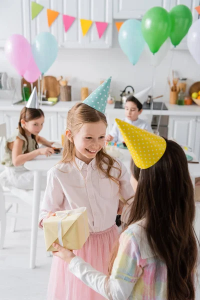 Chica de cumpleaños positiva en la gorra de fiesta recibir regalo de un amigo - foto de stock