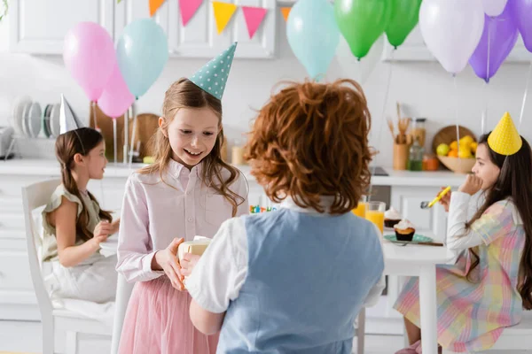 Cheerful girl receiving present from redhead boy during birthday party — Stock Photo