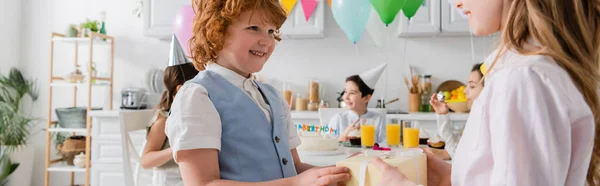 Cheerful girl receiving present from redhead boy near friends during birthday party, banner — Stock Photo