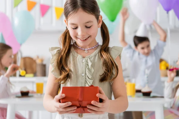 Счастливая девушка с подарком на день рождения рядом с друзьями на размытом фоне — стоковое фото