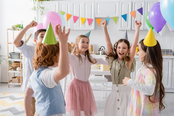 Crianças positivas em bonés de festa se divertindo durante a celebração de aniversário em casa — Fotografia de Stock