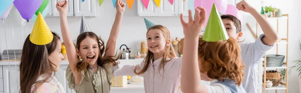 Aufgeregte Kinder in Partymützen, die bei der Geburtstagsfeier zu Hause Spaß haben, Banner — Stockfoto