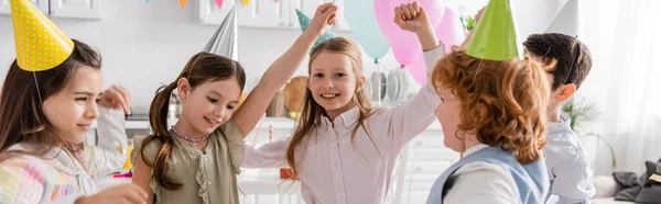 Crianças alegres em bonés de festa dançando durante a celebração de aniversário feliz em casa, banner — Fotografia de Stock