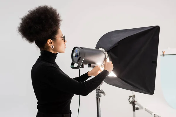 Seitenansicht eines afrikanisch-amerikanischen Content-Herstellers, der Scheinwerfer und Softbox im Fotostudio montiert — Stockfoto