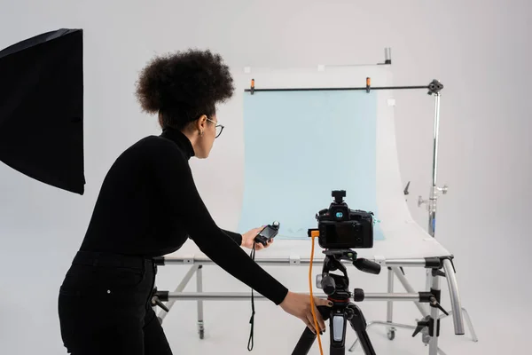 Африканский производитель контента держит измеритель экспозиции рядом с цифровой камерой и столом для съемок в современной студии — стоковое фото