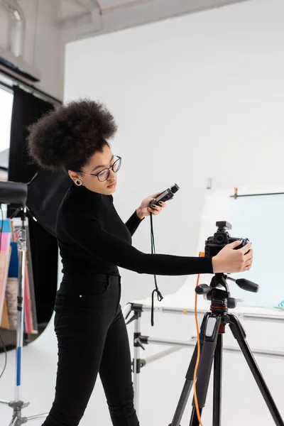 African american content producer with exposure meter adjusting digital camera in contemporary photo studio — Stock Photo