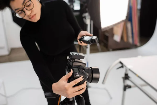 Blurred african american content manager adjusting digital camera while holding exposure meter in photo studio — Stock Photo