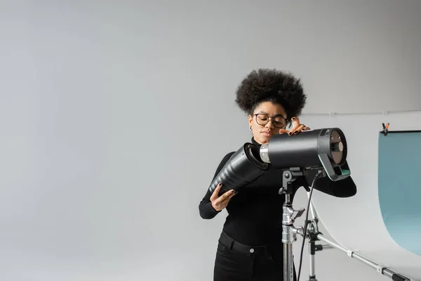 Africano americano gerenciador de conteúdo montando lanterna estroboscópica enquanto trabalhava no estúdio de fotos — Fotografia de Stock