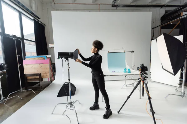 Producteur de contenu afro-américain assemblant des équipements d'éclairage dans un studio photo moderne et spacieux — Photo de stock