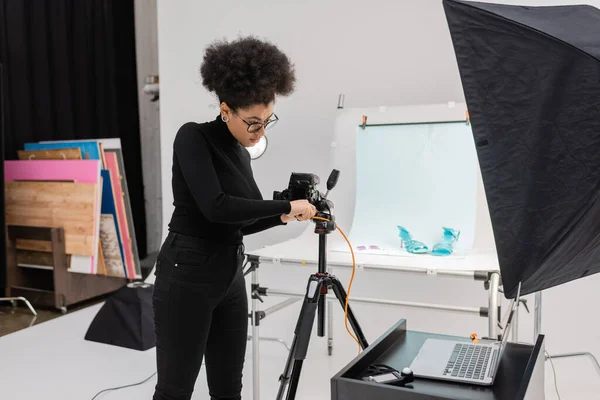 Productor de contenido afroamericano conectar la cámara digital a la computadora portátil en el estudio de fotos moderno - foto de stock