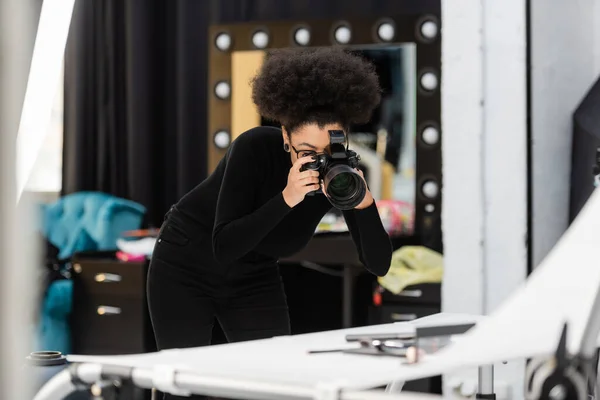 Fabricante de conteúdo americano africano tirar foto de cosméticos decorativos na mesa de tiro borrada no estúdio de fotos — Fotografia de Stock