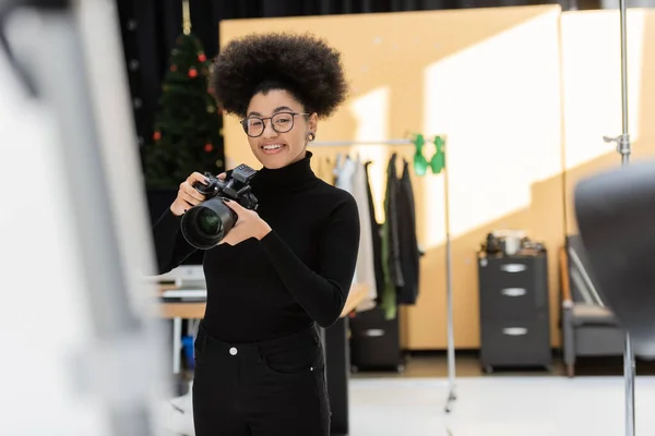 Piacere afroamericano fotografo in piedi con fotocamera digitale professionale in studio fotografico — Foto stock