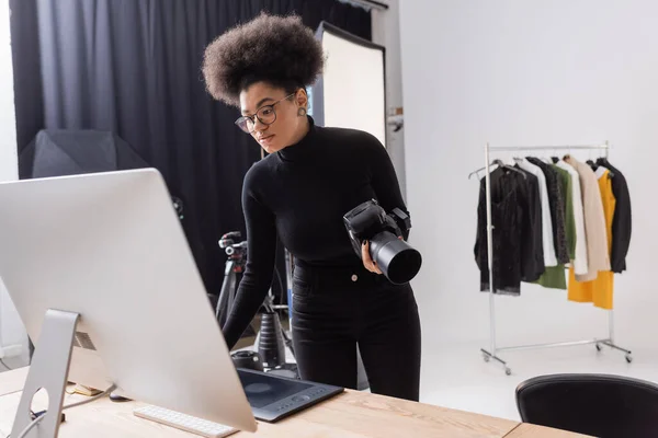 Gestionnaire de contenu afro-américain debout avec appareil photo numérique près du moniteur d'ordinateur dans le studio photo — Photo de stock