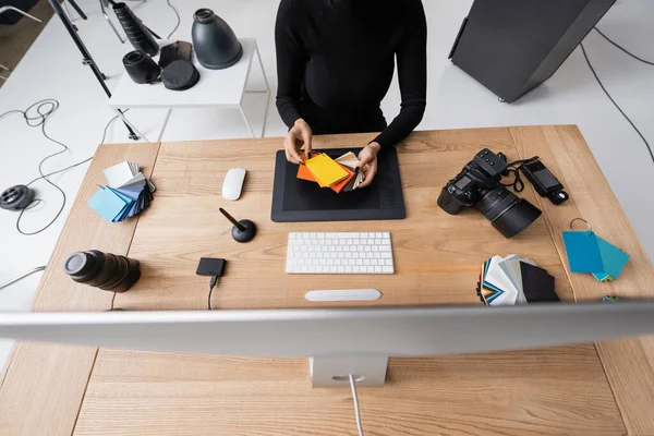 Vue du dessus de la retouche afro-américaine recadrée en choisissant des couleurs près de l'écran de l'ordinateur et la tablette graphique dans le studio photo — Photo de stock