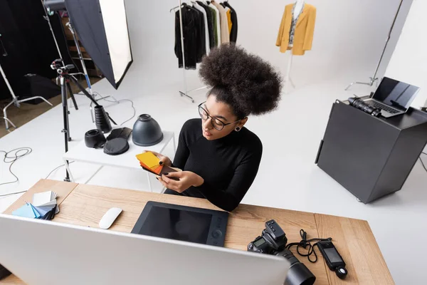 Vista de alto ângulo do retocador afro-americano escolhendo cores perto do computador e tablet gráfico no estúdio de fotos — Fotografia de Stock