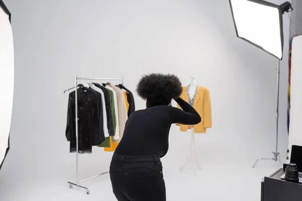 Visão traseira do fotógrafo americano africano tirando foto da coleção de roupas na moda no estúdio de fotos — Fotografia de Stock