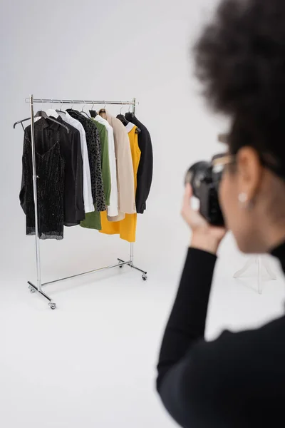 Fotografo afroamericano offuscata scattare foto di vestiti alla moda su rack ferroviario in studio fotografico — Foto stock