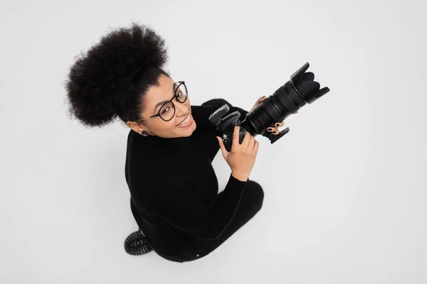 Draufsicht des überglücklichen afrikanisch-amerikanischen Content-Produzenten in Brille mit professioneller Digitalkamera isoliert auf grau — Stockfoto